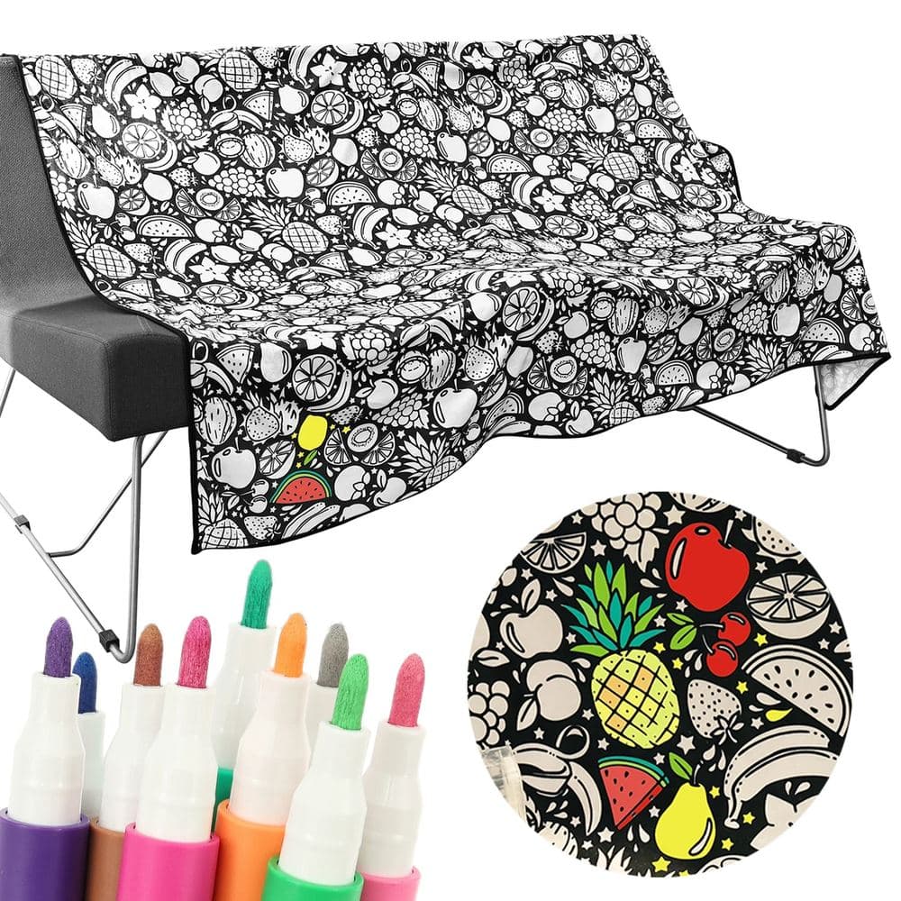 Plaid à colorier Motif du soir : polaire noire imprimée de fruits blancs au trait, posée sur un canapé, avec des marqueurs de couleur et un détail colorié